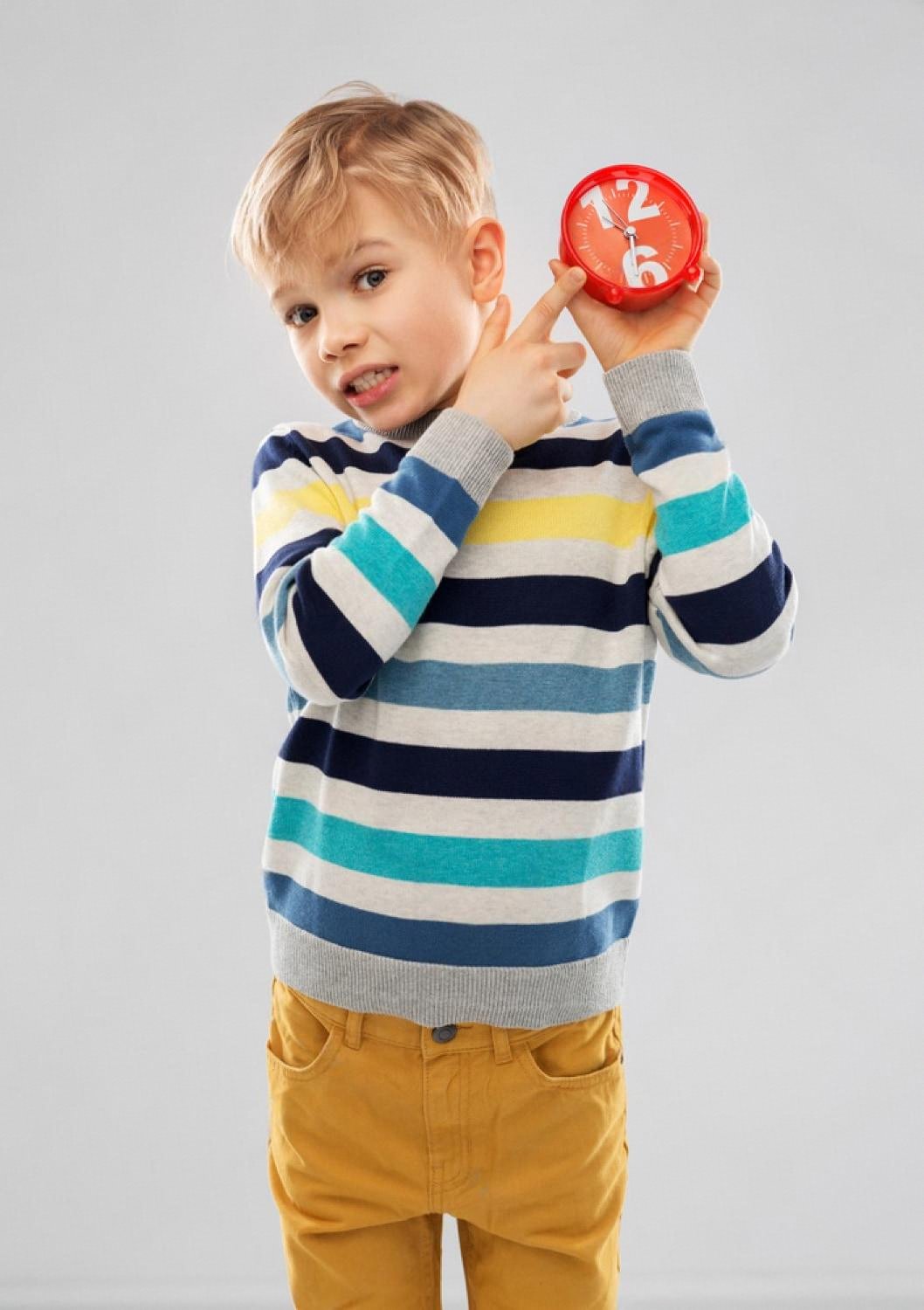 Young boy in a striped sweater pointing at a small red alarm clock