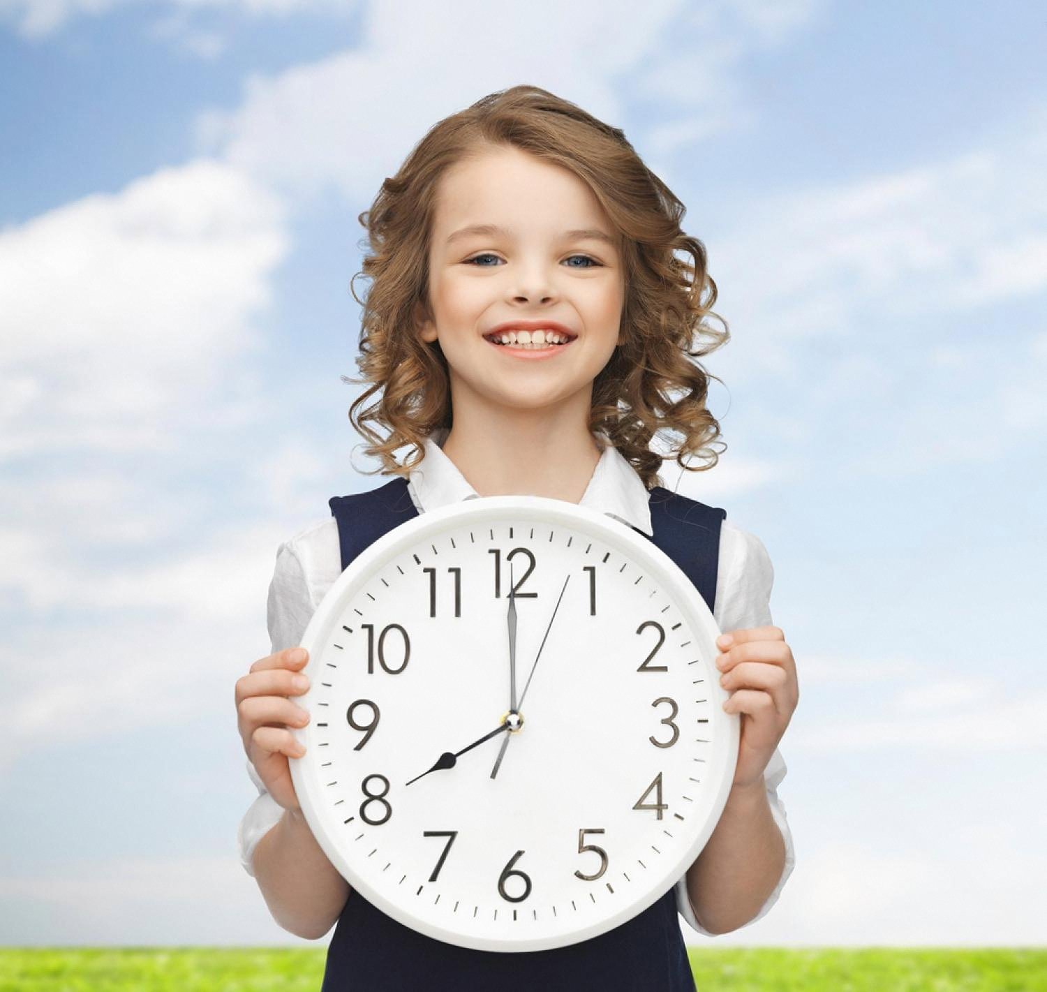 Smiling girl in school uniform holding a large white clock against a bright sky
