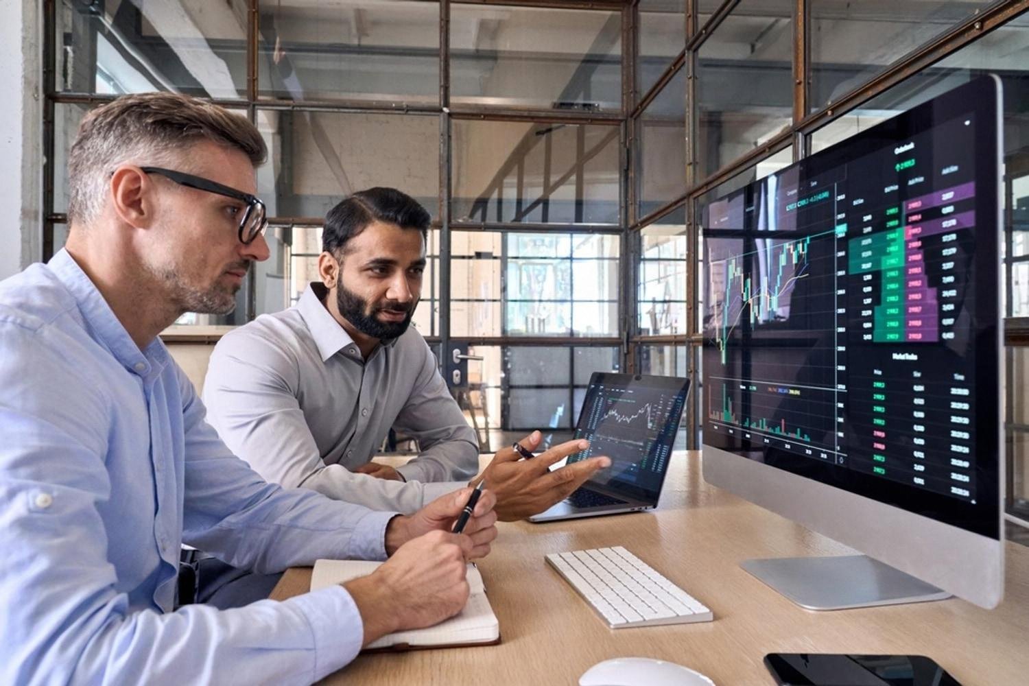 Two business partners analysing market risk data on screens in a Dubai office